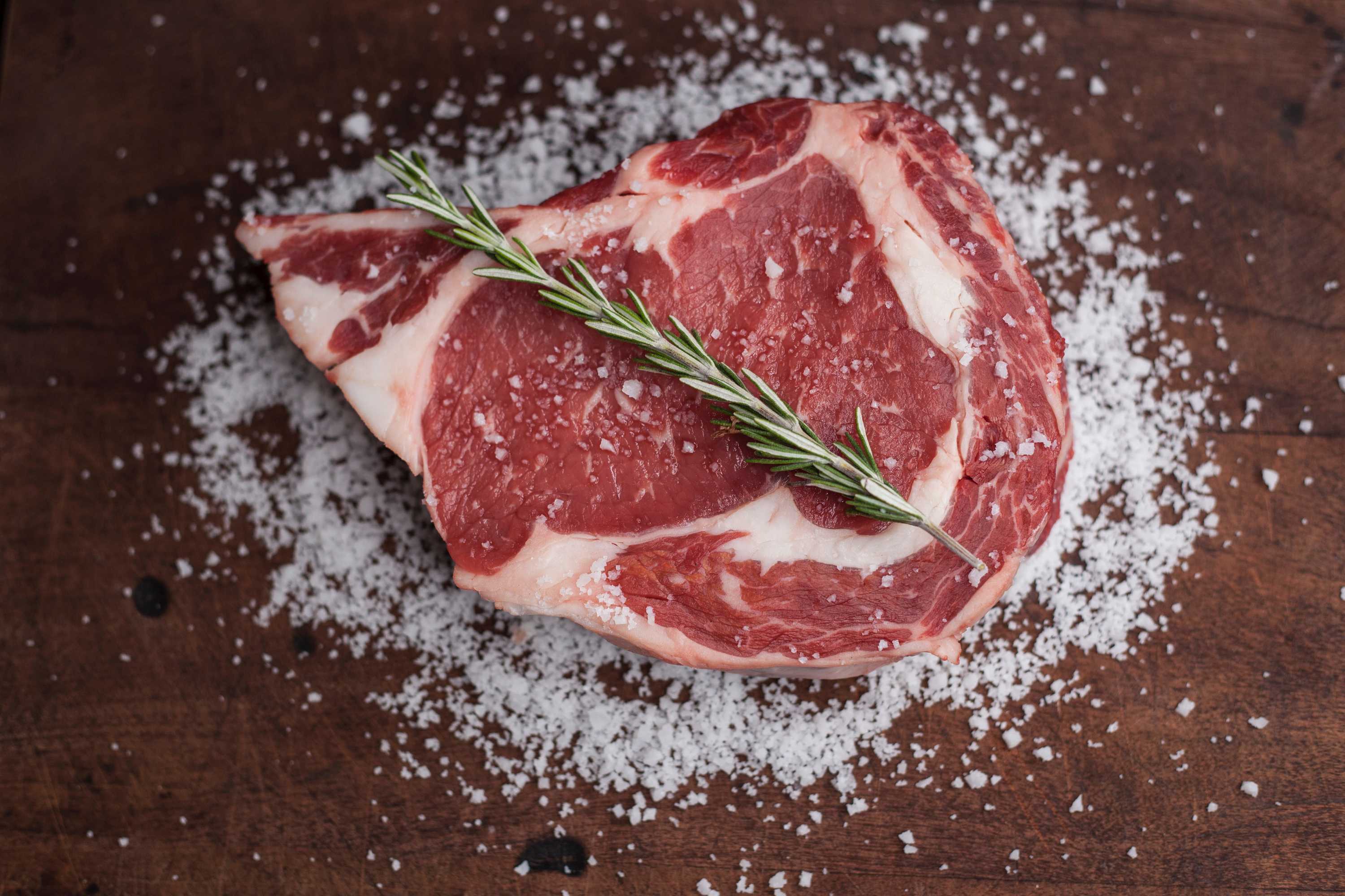 A raw steak topped with a sprig of rosemary lies on a bed of rock salt.