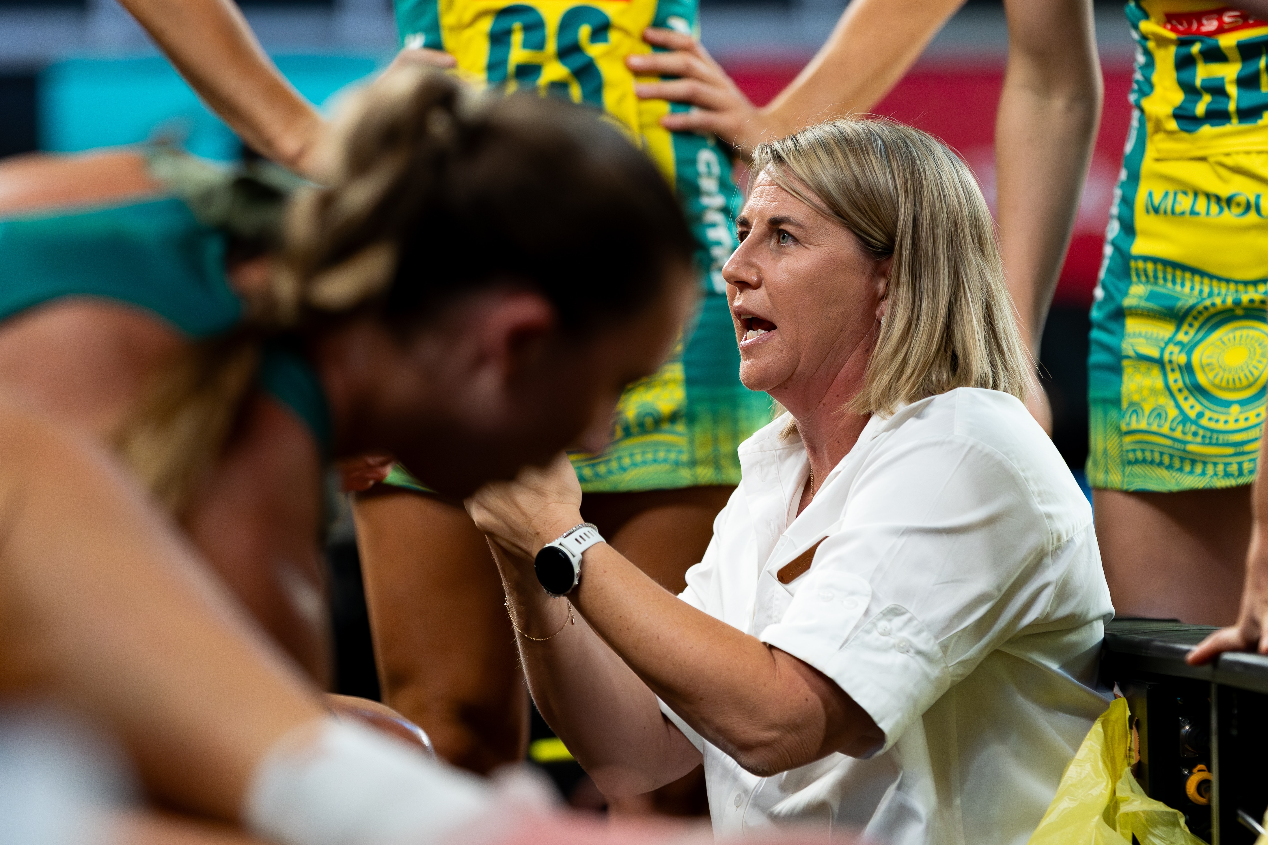 Stacey Marinkovich talking to netball players in yellow and green dresses. 