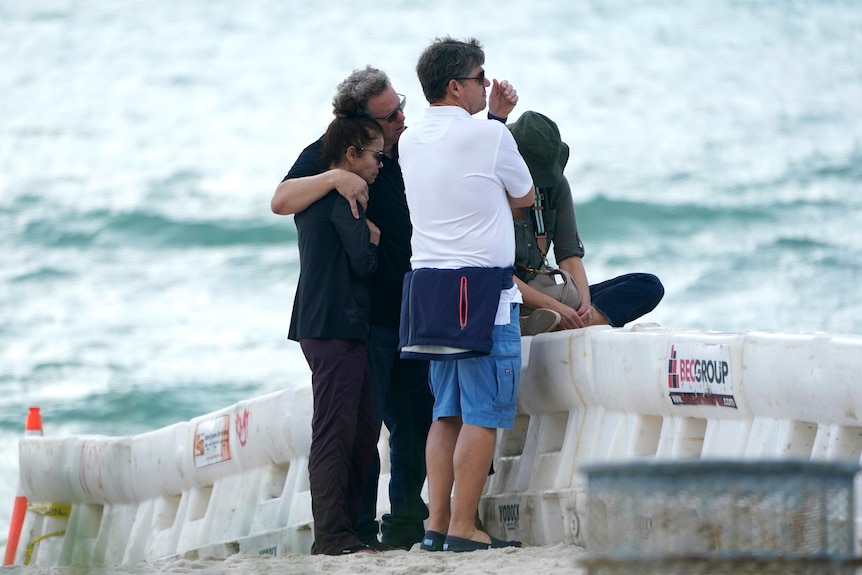 A group of people stand behind a barricade on the beach near the Champlain Towers South