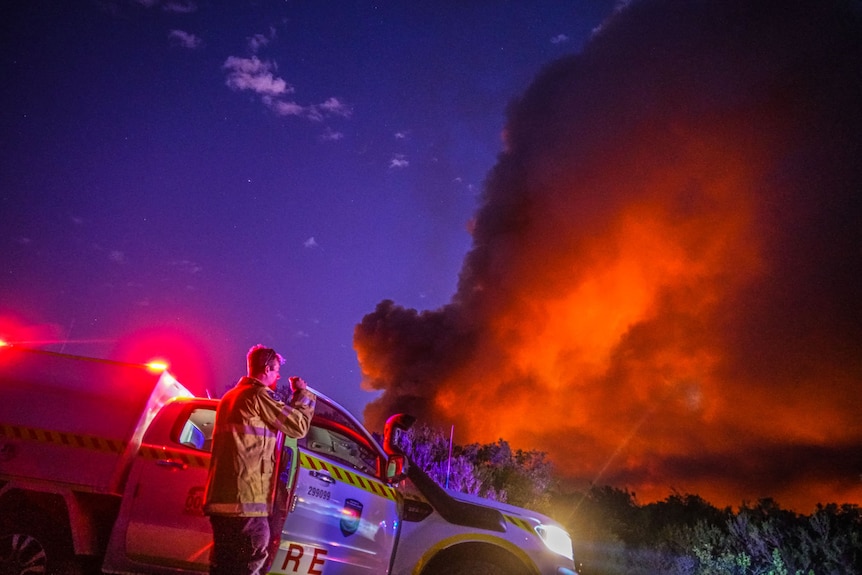 A firefighters takes a photos of smoke and flames at night