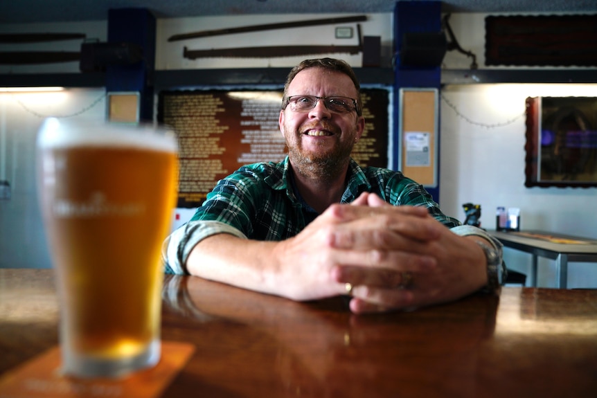 Man sits at a bar, with a freshly poured cold beer in front of him
