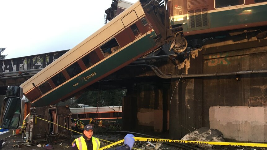 A derailed train carriage hangs off a bridge.