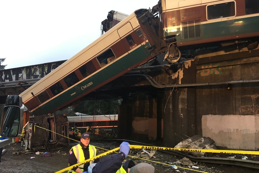 A derailed train carriage hangs off a bridge.