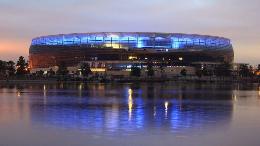 New Perth stadium illuminated in blue as the sky lightens, view from across the river.