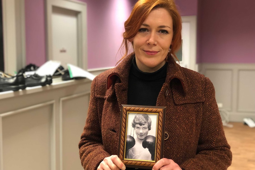 Julieann Campbell wears a maroon coat and black turtleneck as she holds a black and white portrait of her boxer uncle.