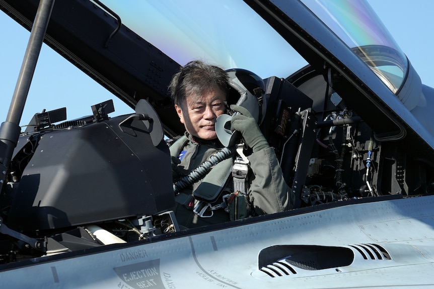 Moon Jae-in sits in a jet and points out of the cockpit. 