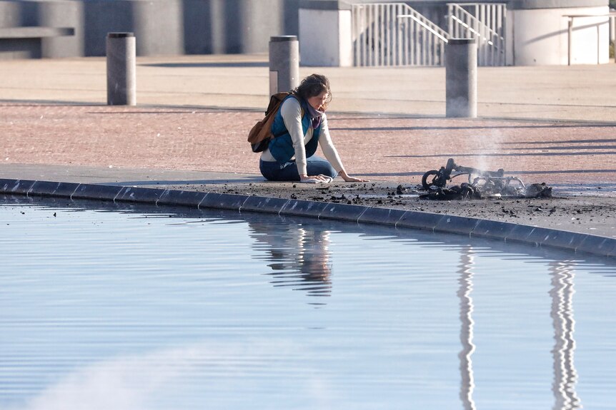 a woman sits on the ground along a smouldering pram on the forecourt of parliament house