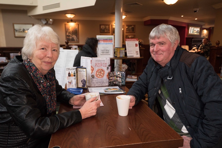 A grey-haired woman and man sit at a table in a pub.