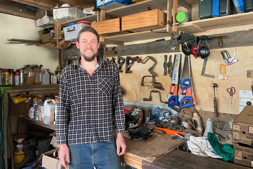 a photo of a guy in flannel shirt standing in front of his work bench and tools 