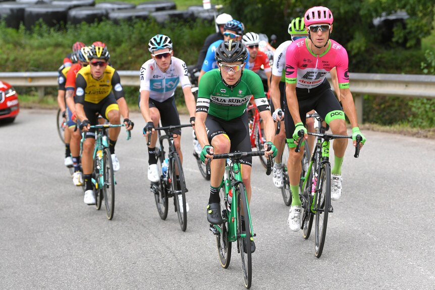 An Australian cyclist in a green shirt rides at the front of a group of about 10 riders during a Tour de France stage.
