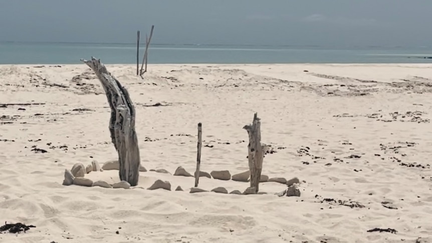An arrangement of stones and sticks on a mound of sand on a beach