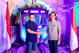 Anies Baswedan smiling and shaking hands with Indonesia's President Joko Widodo with vivid blue and purple train in backgro