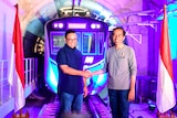 Anies Baswedan smiling and shaking hands with Indonesia's President Joko Widodo with vivid blue and purple train in backgro