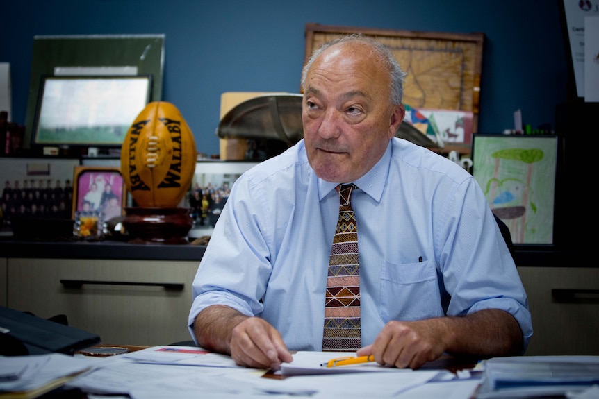 Michael Freelander sits at a desk covered with papers, in his office.