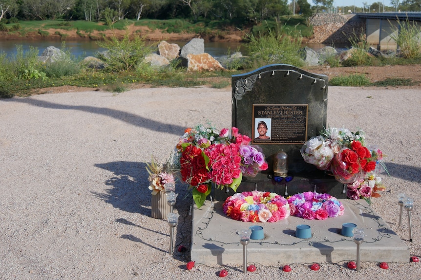 A grave headstone with colourful flowers, sitting on a ledge above a river.