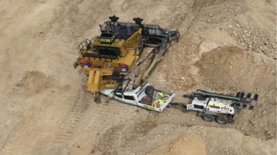 A white ute crushed under heavy machinery at a mine site.