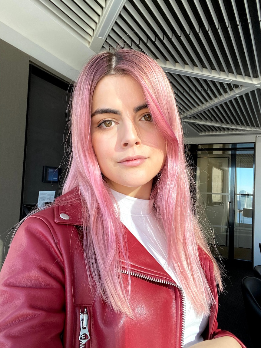 Portrait of a young woman with pink long hair and a dark pink jacket.