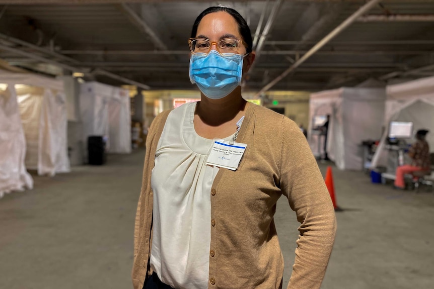 A woman in a blue face mask stands in a covered car park