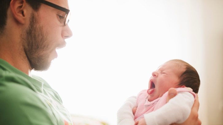 Picture of dad holding baby: dad has an open mouth and the baby has its tongue out, possibly yawning