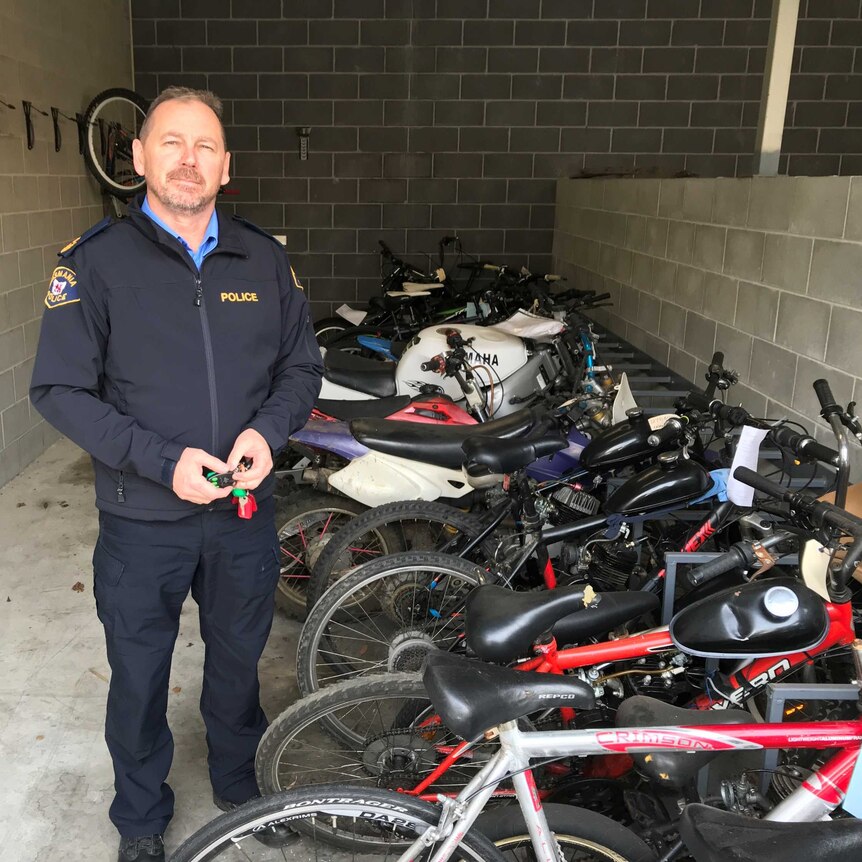 Senior Sergeant Michael Foster of Tasmania Police in front of many motorcycles and pushbikes