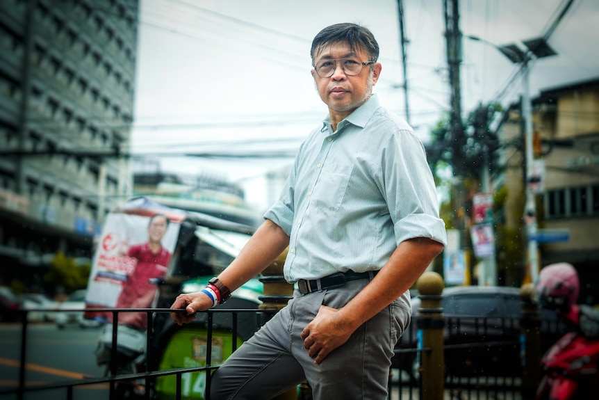 A man with bushy white chops stands on a street corner in the Philippines 