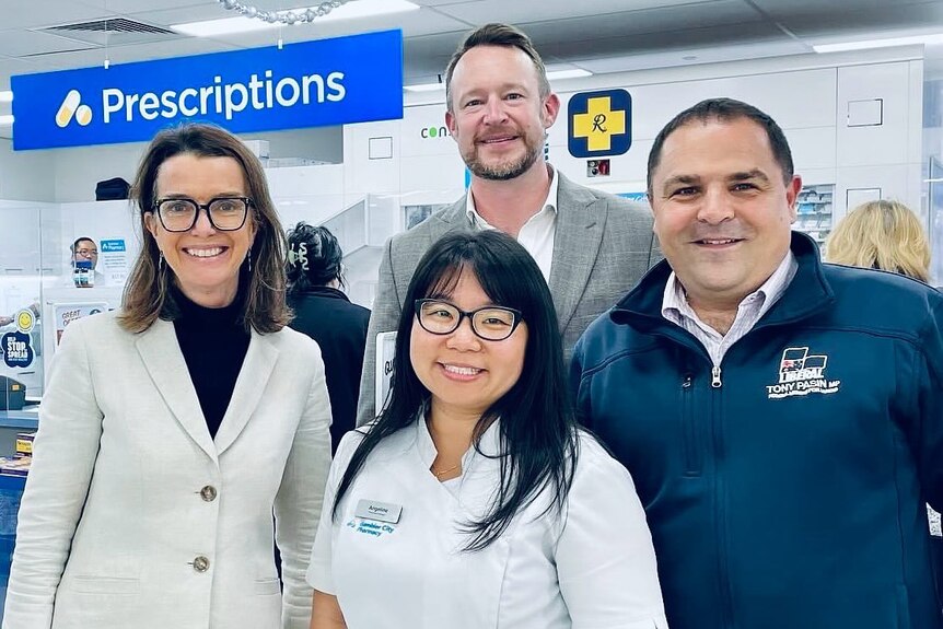 Two women and two men standing in a pharmacy with a sign saying "prescriptions".