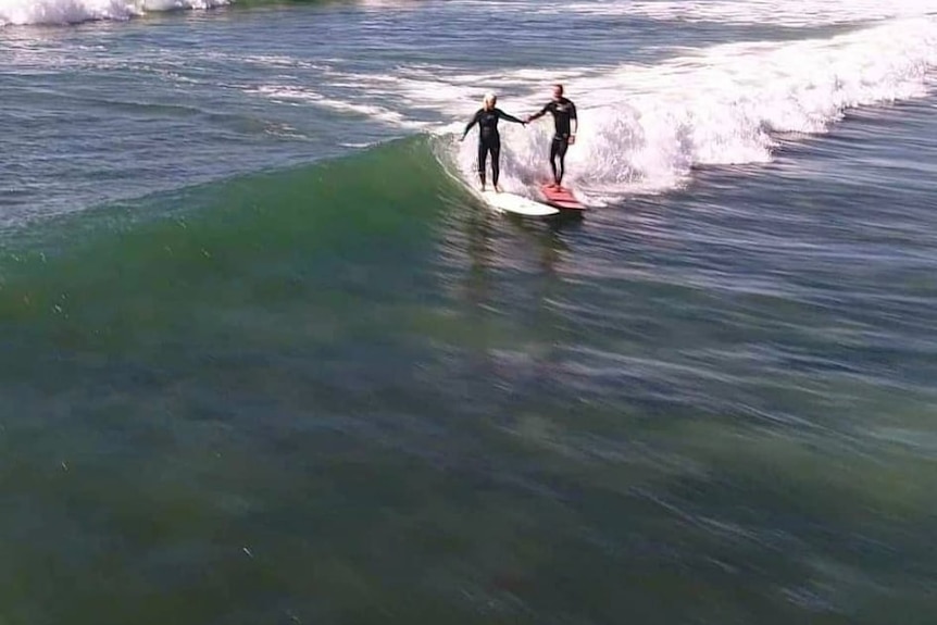 Two people holding hands while riding a wave