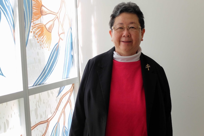 Josephite Sister Margaret Ng standing next to window painted with gumnuts and leaves.