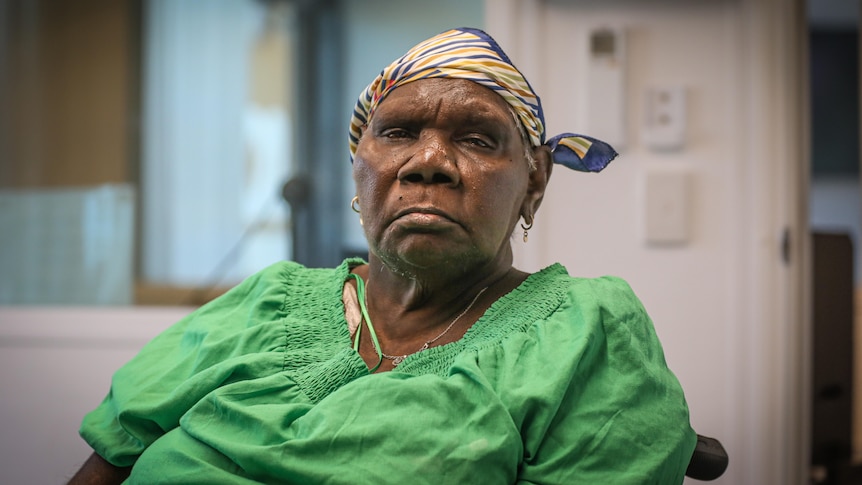 Image of an Indigenous woman, wearing a green shirt and head scarf, sitting in a chair