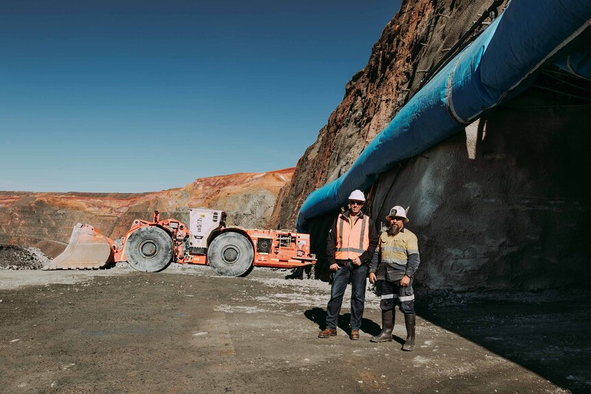 Two men wearing high-vis workwear standing near parked machinery at a gold mine.  