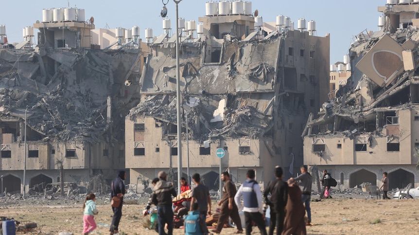 buildings in ruin in the background as people stand around in the foreground