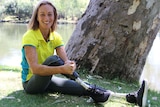 Para-athlete Eliza Ault-Connell sits on grass in front of a tree with river in background.
