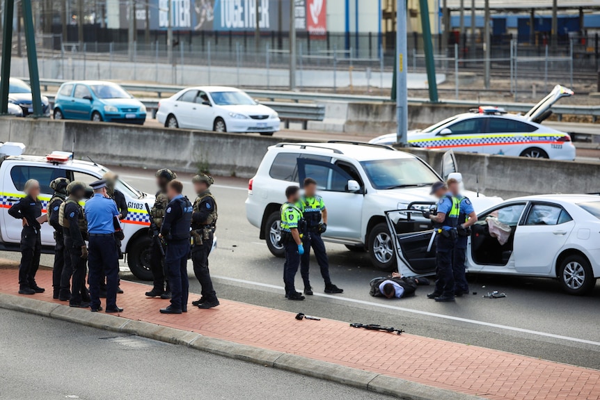 Police stand around a man in front of crashed cars.