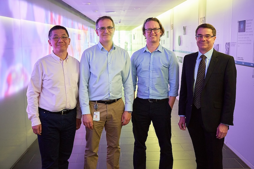 Four men in businesswear stand in a hallway