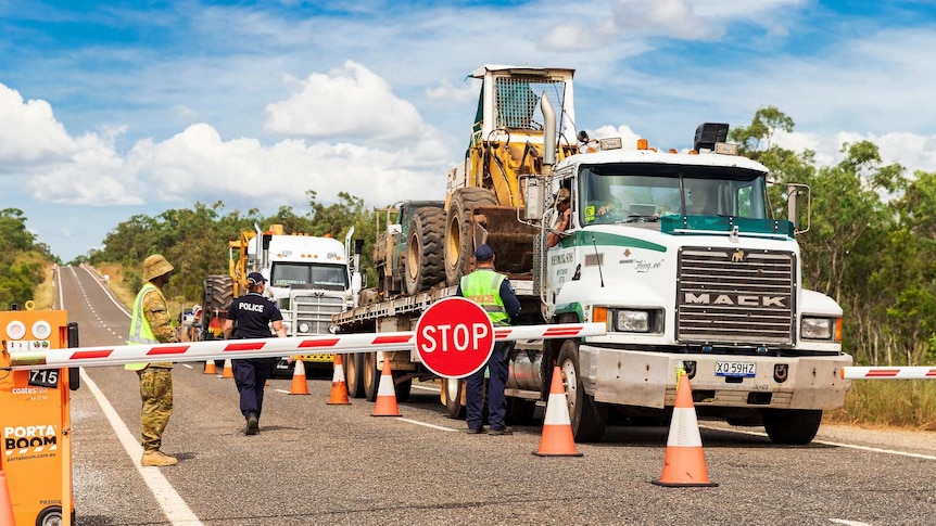 Trucks stopped in front of boom gate with police and ADF personnel standing on the road