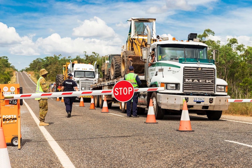 Trucks stopped in front of boom gate with police and ADF personnel standing on the road