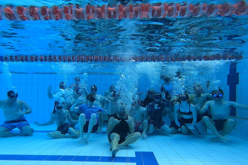 A group of about 20 people blowing bubbles on the bottom of a pool.