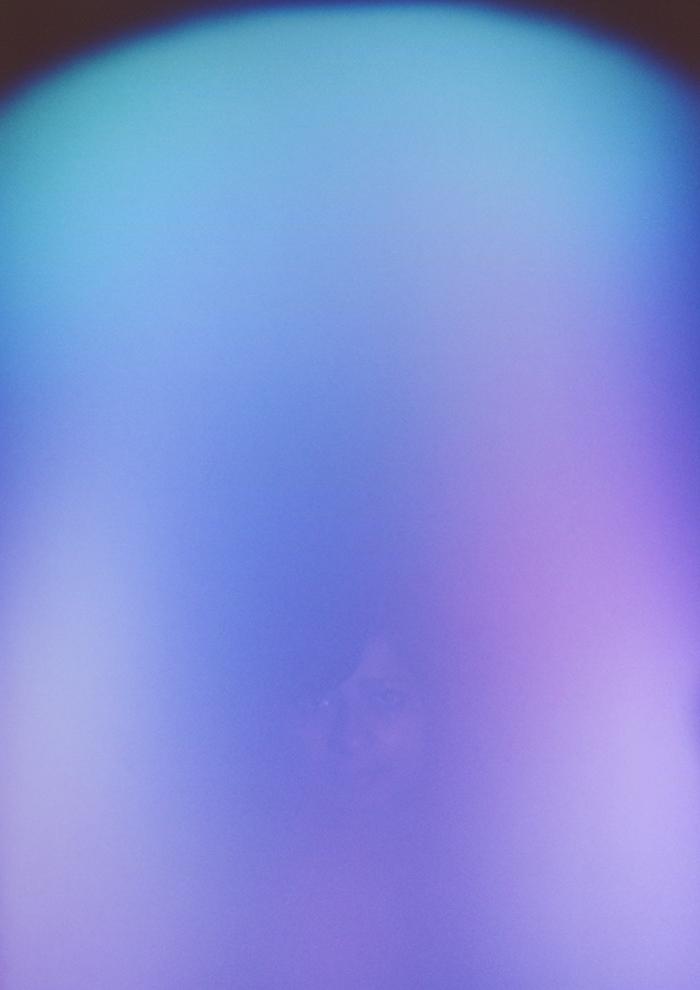A faint image of a woman with dark hair and side fringe sits under a strong wash of white, blue and purple colours.