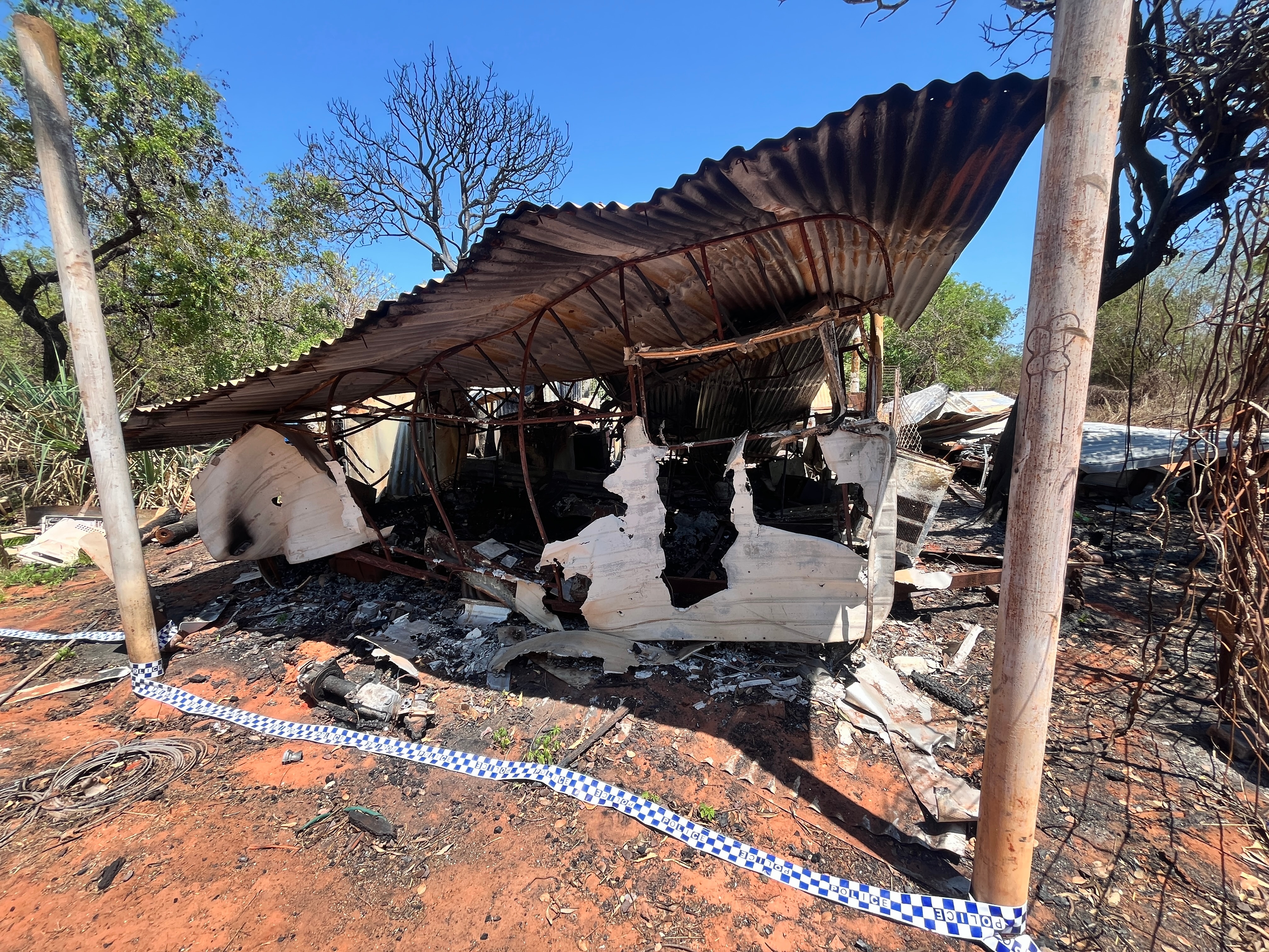 The mangled remains of a shed in an outback area. Police tape lies on the the ground around its perimeter.
