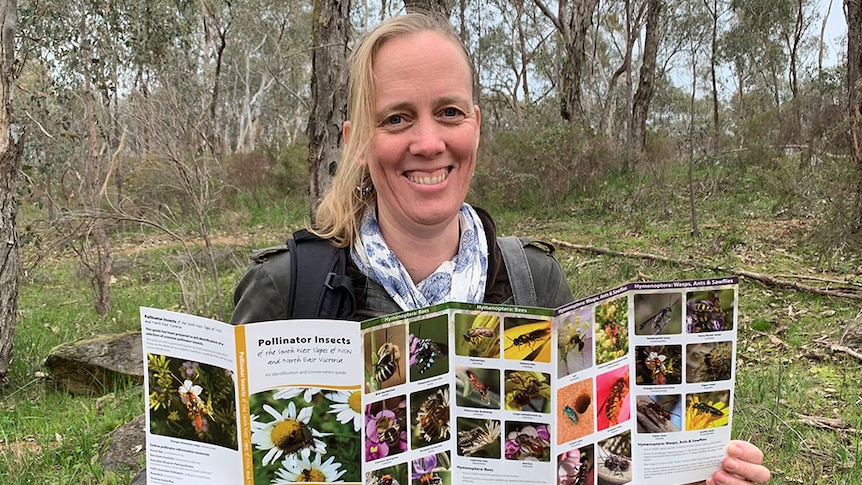 Woman looks at camera, smiling and holding onto a pollinator guide.