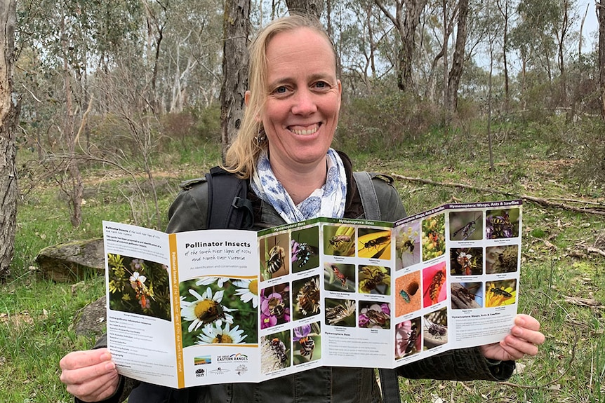 Woman looks at camera, smiling and holding onto a pollinator guide.