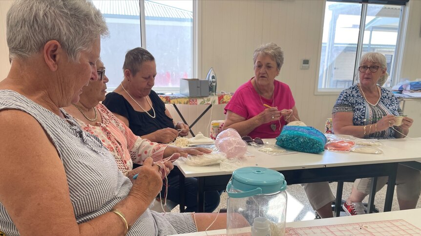Five women sit around a table knitting