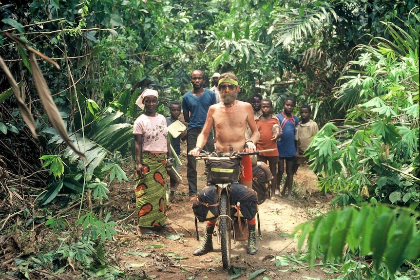 Shirtless man on bicycle in jungle with African woman, man and children