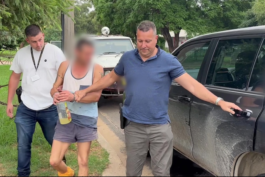 A man being escorted into a car by two police officers