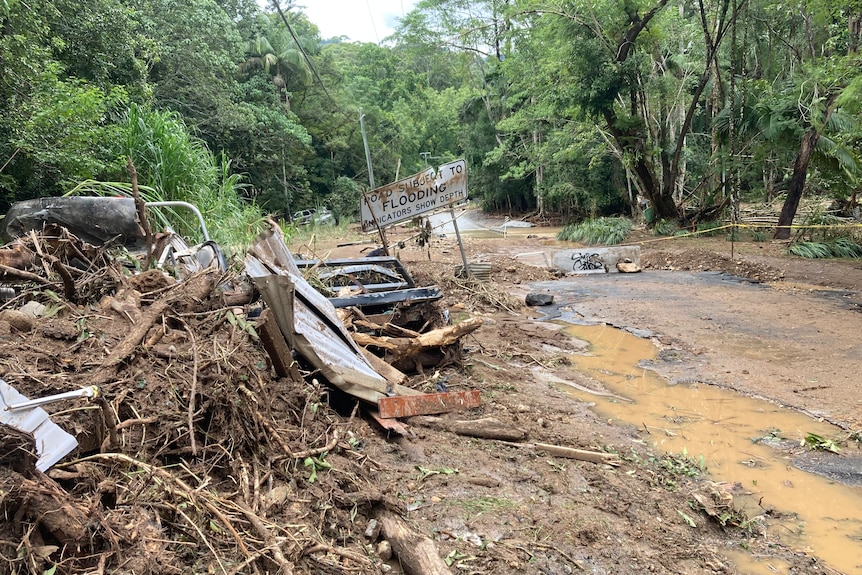 A road partially covered in water with rubble on one side and a sign.