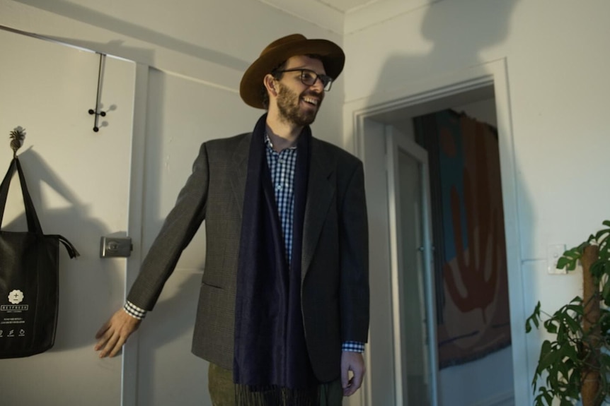A man in a hat and glasses standing by a door in an apartment