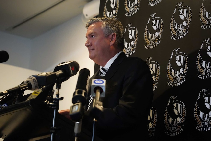 Side-on of Eddie McGuire behind microphones and a lectern.