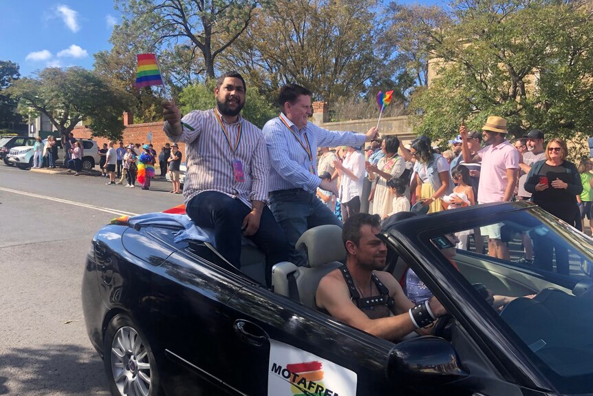 A man waves a rainbow flag in a topless car