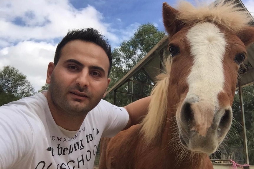 A man with black hair poses with a horse