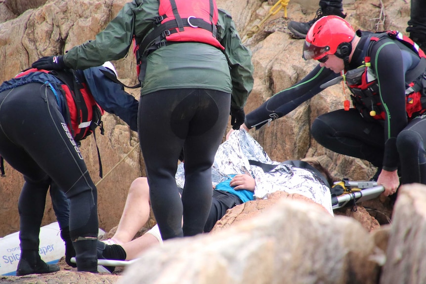 Three people lean over a boy covered in an emergency blanket on a stretcher